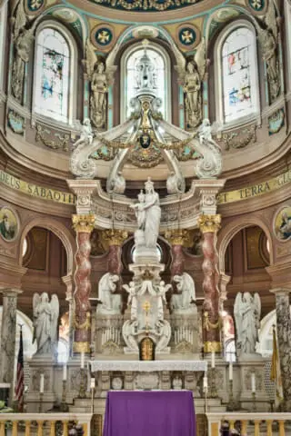 The focal point of the altar is a nine-foot marble statue of the Blessed Mother which was personally blessed by Pope Pius XI before being shipped to the United States. A gracefully unfurled canopy supports a large gold cross held aloft by four angels.